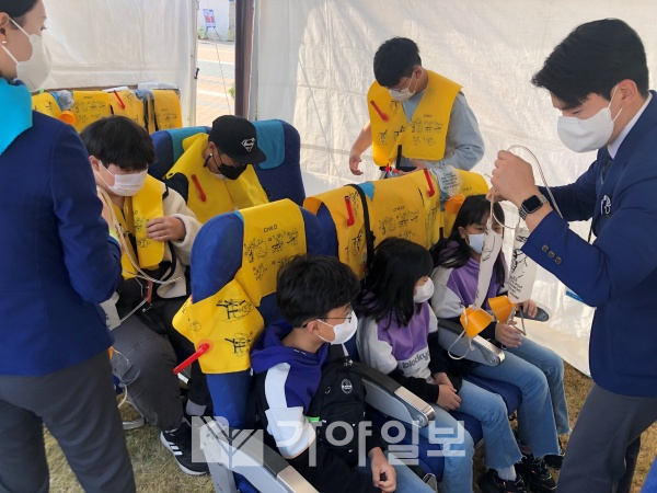 사진2)에어부산 직원이 기내 안전 체험 부스에 방문한 지역민들에게 기내 안전 장비 착용법을 알려주고 있다.